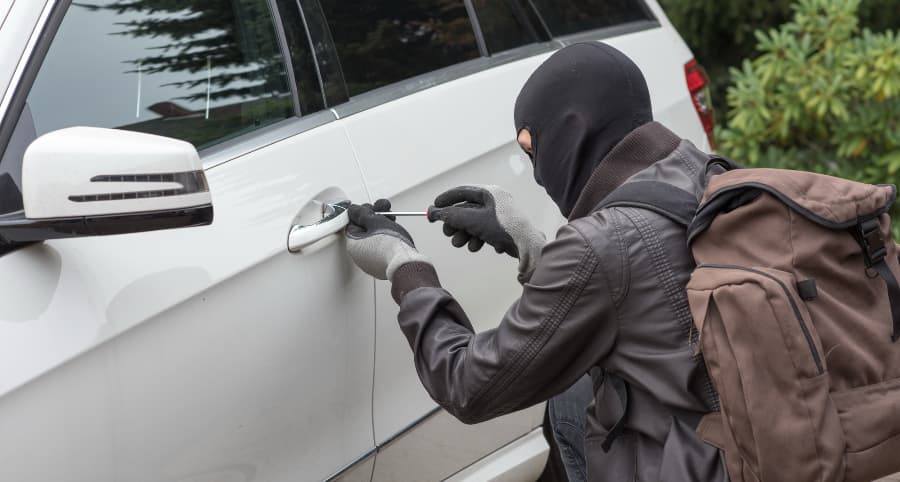 Thief trying to break into a white automobile in a residential neighborhood